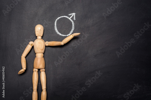 Wooden man stands next to a drawn icon Male sign on a chalk board