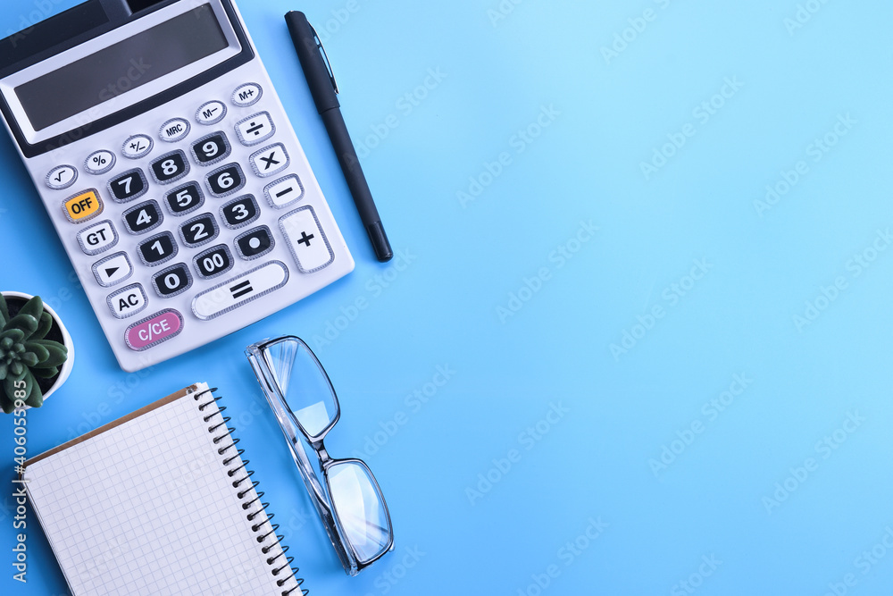 Calculator keypad on a blue background.Notebook, pen, glasses, desktop. Finances Top view. Copy space