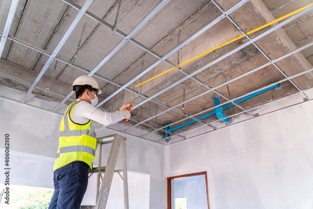 custom made wallpaper toronto digitalElectrician wearing a mask installing laying electrical cables on the ceiling with pliers inside the house under construction.