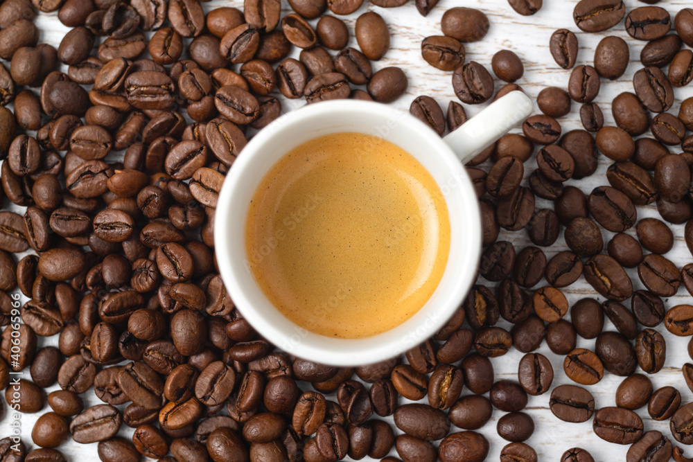 Fototapeta premium Cup of espresso surrounded with a lot of roasted coffee beans on a white wooden background.