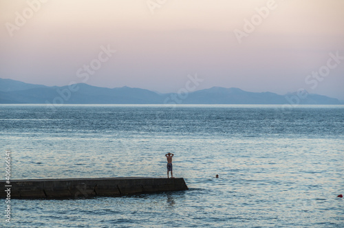 a man stands on a pier by the sea and looks into the distance at the pink sky, seeing off the sunset