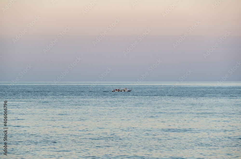 a boat sails in the middle of the sea against a pink sky at sunset in summer