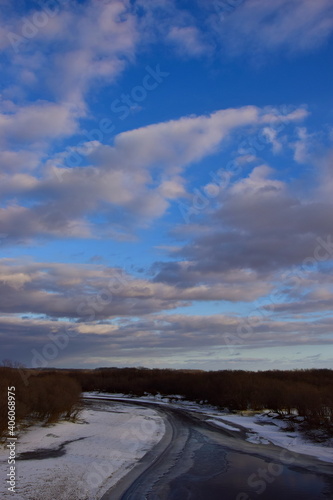 Freezing river in november. Ice on the banks. Blue sky with gray clouds at sunset.