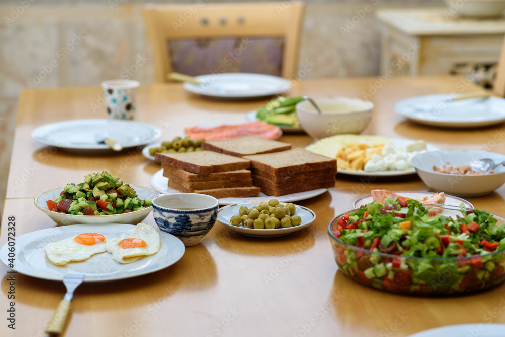 Serving of eggs, bread and salad from fresh vegetables on a wooden table, healthy and organic food, breakfast with friends.