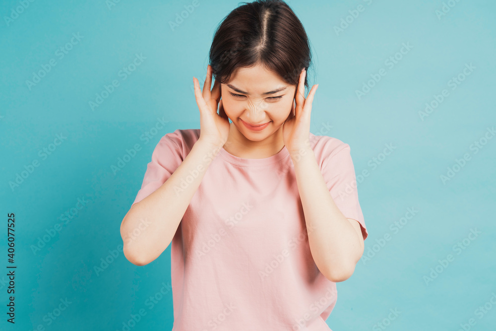Portrait of girl covering ears and feeling discomfort on blue background Portrait of girl covering ears and feeling discomfort on blue background