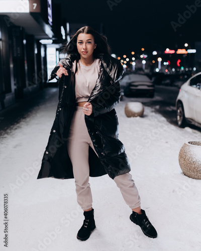 beautiful girl with long dark hair in a black jacket in the winter night on the street