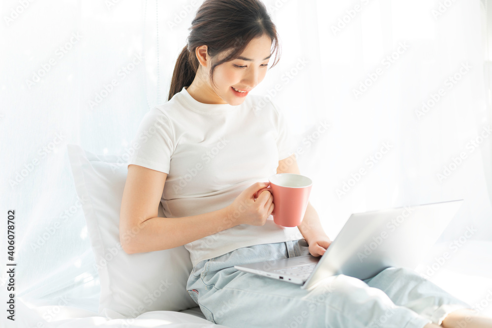 Young Asian woman sitting on bed working watching home entertainment Young Asian woman sitting on bed working watching home entertainment