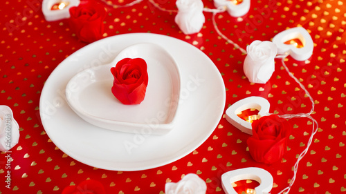 Place setting in red and white - for Valentine or other event. White plate in the shape of a heart with a decor of roses on a red background