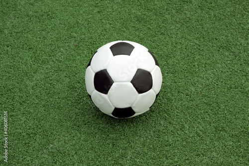  White and black ball for playing soccer lays on green synthetic grass close up view