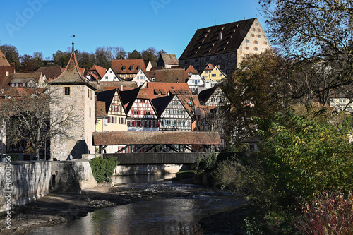 Cityscape of Schwäbisch Hall, Germany with its colorful half-timbered houses, a stone city wall and a wooden bridge that is leading over a river.