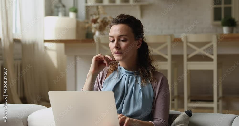 Young attractive concentrated woman sitting on couch working on laptop doing remote freelance tasks looking pensive, solve business issues from home. Creative teleworking activity, brainwork concept