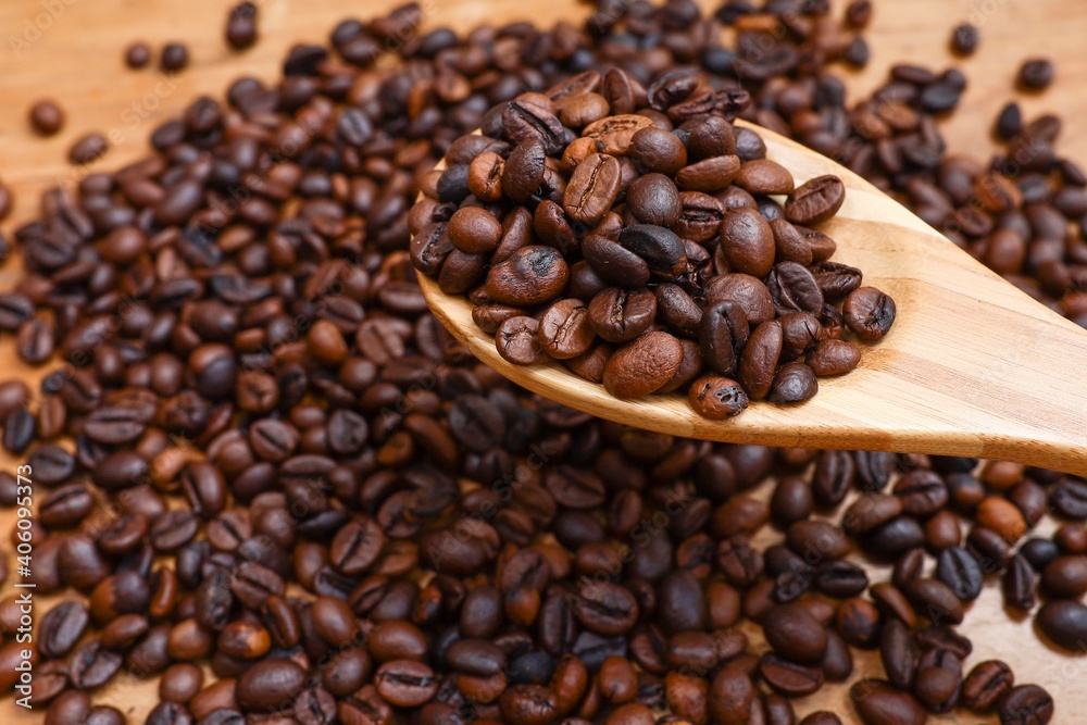 A group of coffee beans in the wooden spoon on top of a pile of coffee beans A group of coffee beans in the wooden spoon on top of a pile of coffee beans