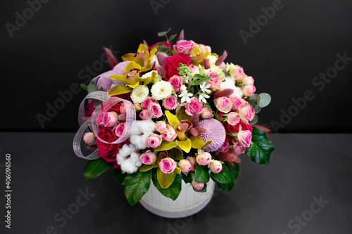 Floral arrangement with orchids, cotton and other flowers in a large hat box on a dark background.