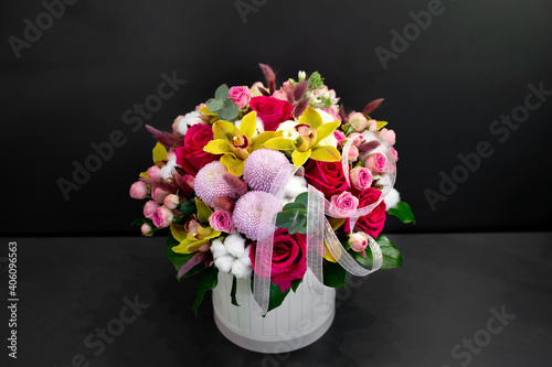 Floral arrangement with orchids, cotton and other flowers in a large hat box on a dark background.