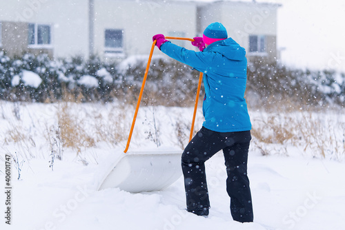 Woman cleaning snow with shovel in winter day. Woman shovelling snow walkway in front of house