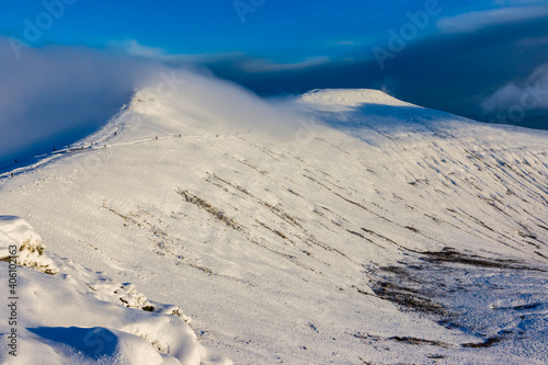 Hikers and walkers on a cold, snow covered mountain in the early morning sunshine (Pen-y-Fan)