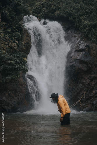 An asian male traveler enjoying the beauty of rainforest waterfall.A male explorer in the waterfall pool.Camping and hiking lifestyle.Into the wild.