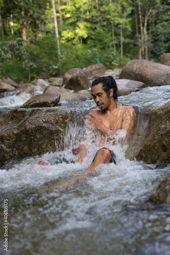 A male traveler enjoying the cold of rainforest stream during morning.Man shower in the waterfall pool.