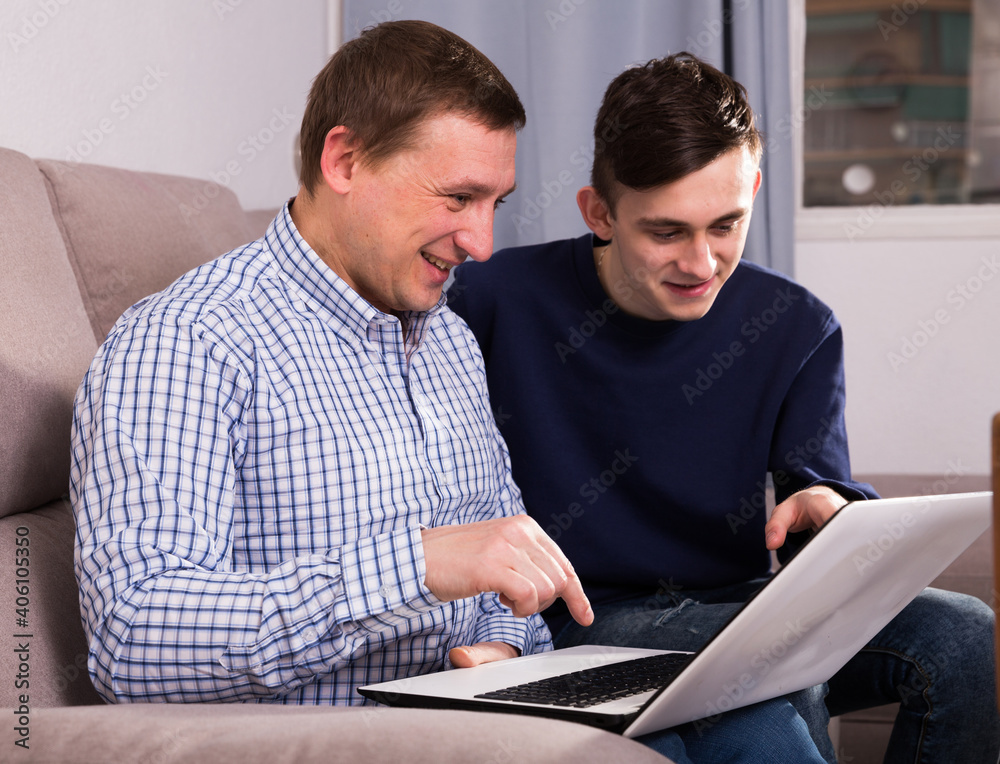 Man with his adult son are playing on laptop together at the home.