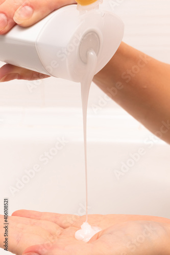 female hands pour shampoo into the palm from a white bottle in a bathroom on a light background