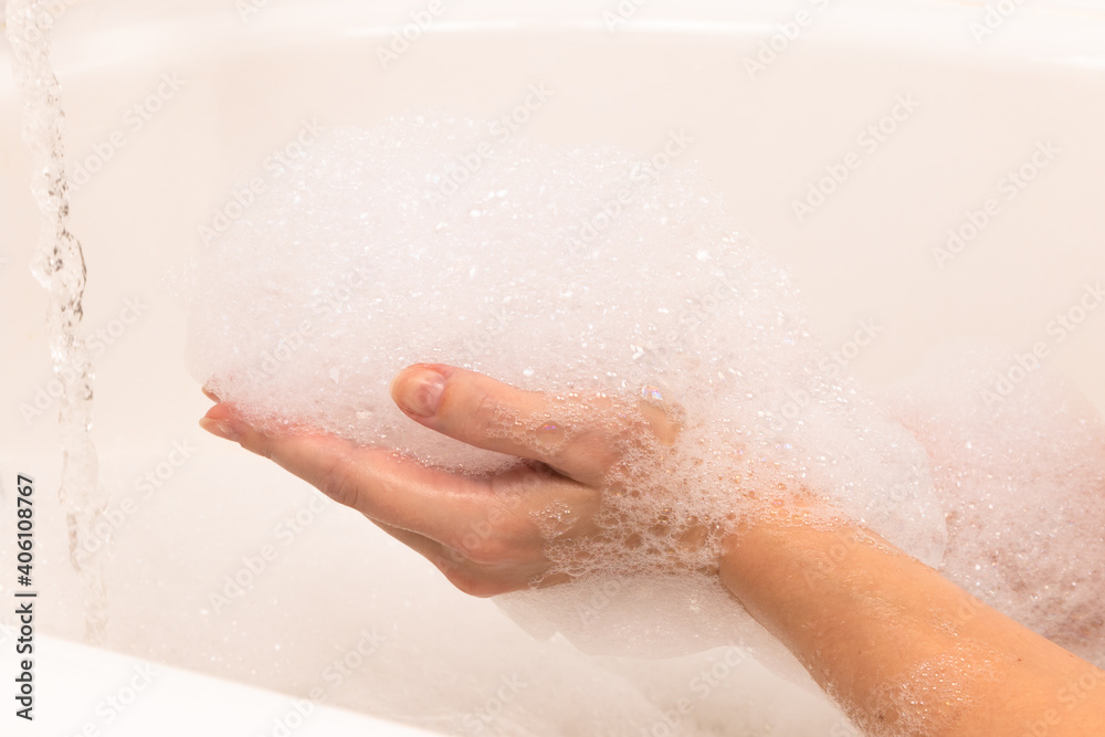 soap foam forms on a woman's hand in the bathroom, a stream of water. background light tile soap foam forms on a woman's hand in the bathroom, a stream of water. background light tile
