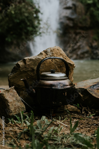 Boiling water in the keetle using camping stove with waterfall in the background.