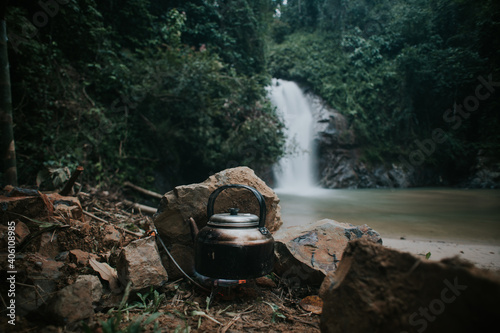 Boiling water in the keetle using camping stove with waterfall in the background.