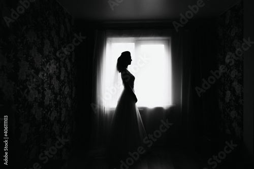 Silhouette of bride in a dress by the window on the wedding day