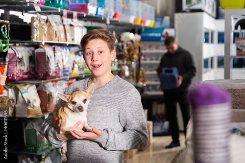 Portrait of happy teen boy with his little dog visiting pet supplies shop. High quality photo