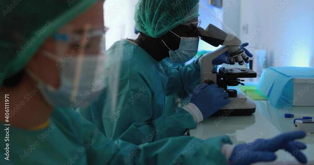 Medical workers in hazmat suit working with laptop computer and micoroscope inside lab hospital during coronavirus outbreak