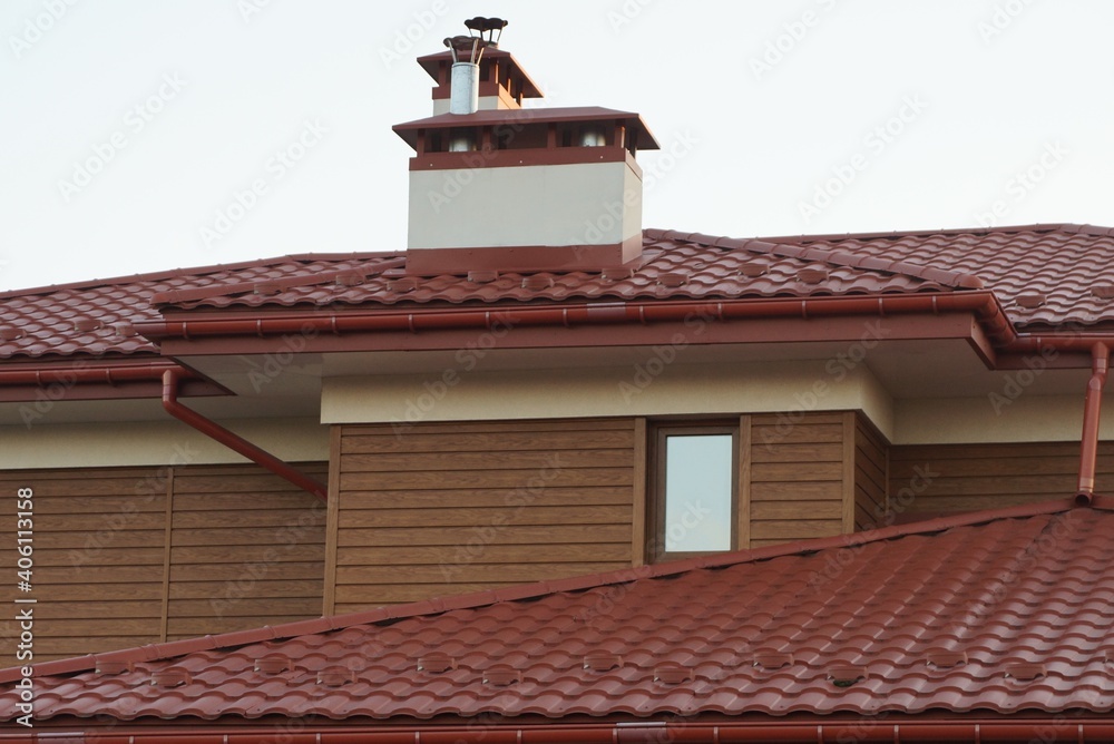 brown wooden attic of a private house with a window and part of a red tiled roof with a chimney against a gray sky