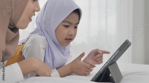 A young beautiful Muslim mother and her daughter are talking and enjoying watching content within a tablet computer, a modern lifestyle Muslim family, a young mother with a lovely daughter.
