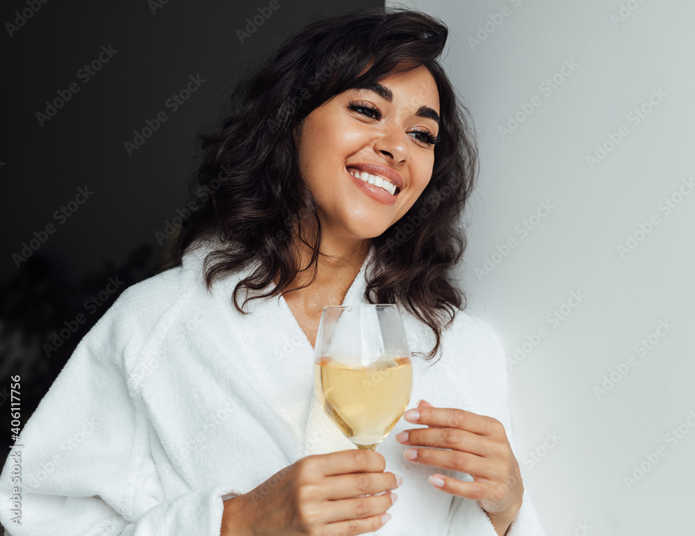 Young brunette female in a white bathrobe standing next to a window and holding a wine glass Young brunette female in a white bathrobe standing next to a window and holding a wine glass