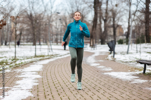 Fit sportswoman running on path in park on snowy winter day. Recreation, snowy weather, winter day