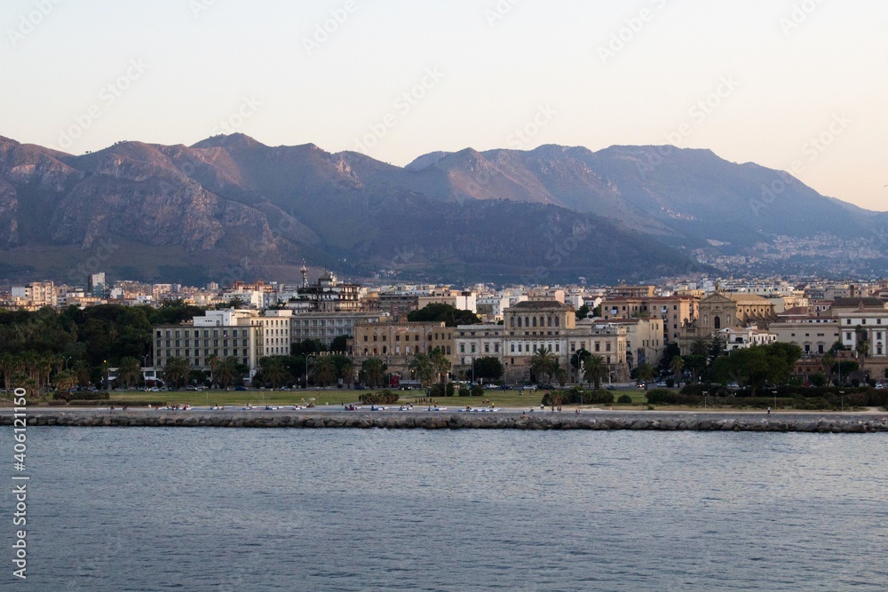 evocative image of the view of the city of Palermo from a ferry with the mountains in the background at sunset
