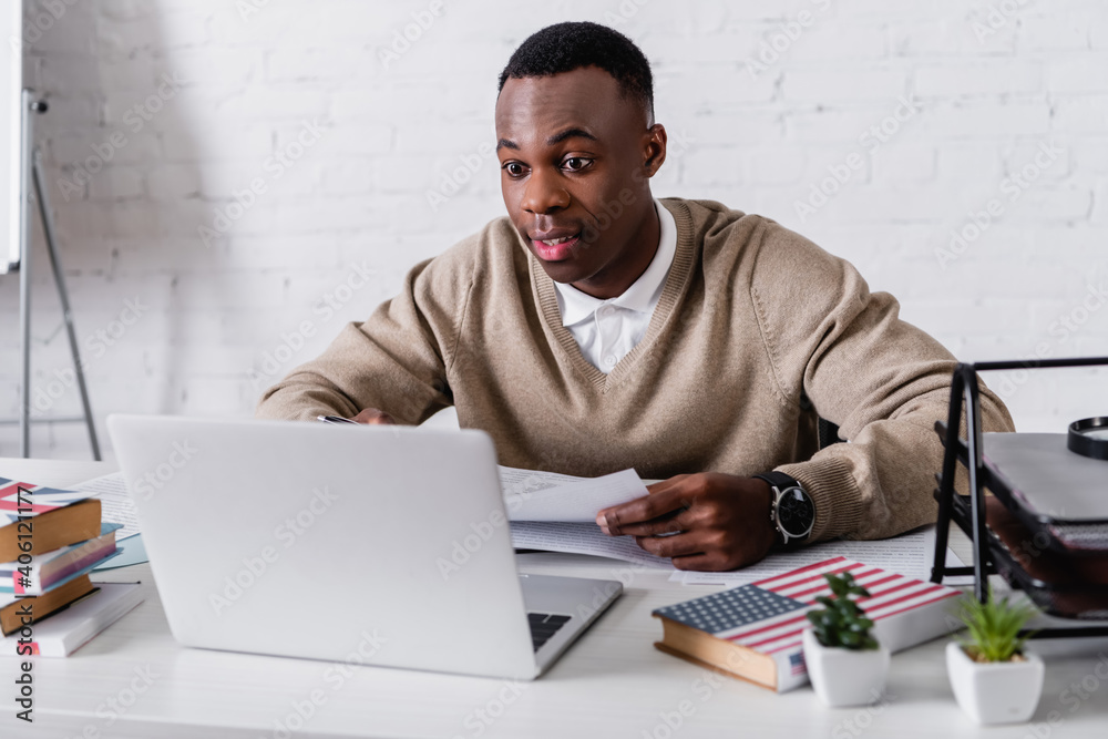 amazed african american translator working at laptop near dictionaries on blurred foreground amazed african american translator working at laptop near dictionaries on blurred foreground