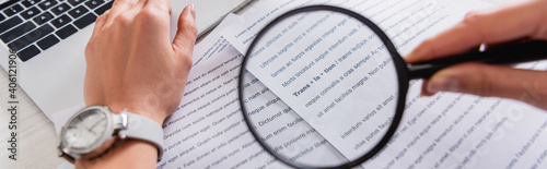 cropped view of translator holding magnifying glass near documents with english text, banner photo