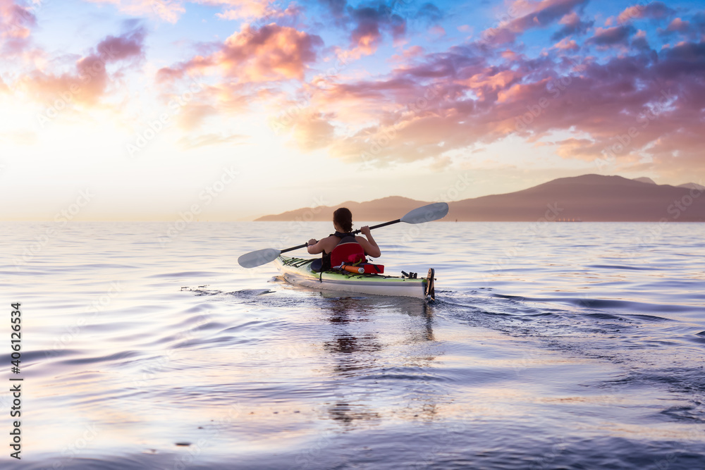 Woman on a sea kayak is paddling in the ocean during a colorful and vibrant sunset. Taken in Jericho, Vancouver, British Columbia, Canada. Concept: Adventure, Holiday, Vacation, Lifestyle, Freedom