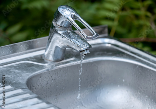 Defective faucet. Cause wastage of water. Water tap outdoor green park background. Please, save water