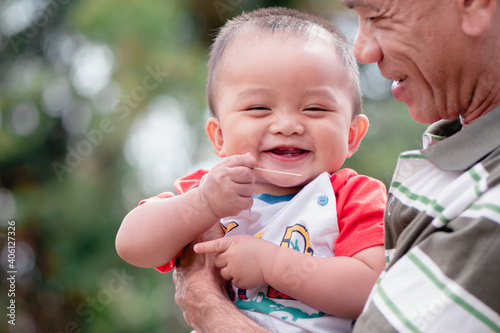 Portrait of adorable expressions of Asian little baby and grandfather on nature background with copy space,Cute boy, 7 months old, crawling age, good smile and good mood. Healthy, big black eyes.