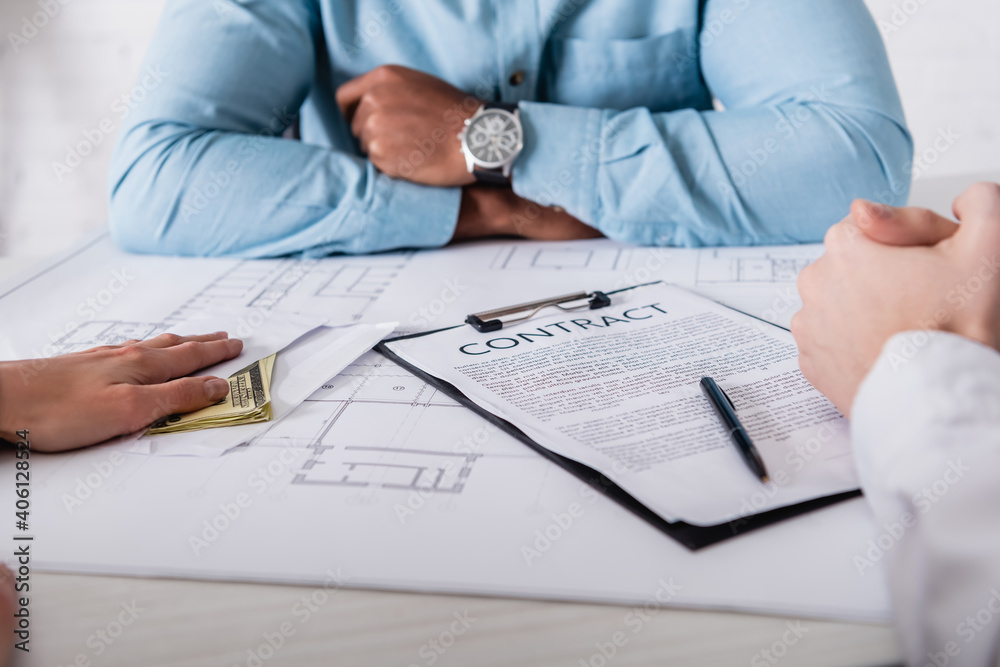 cropped view of woman giving bribe to african american businessman near blueprint and contract, blurred background cropped view of woman giving bribe to african american businessman near blueprint and contract, blurred background