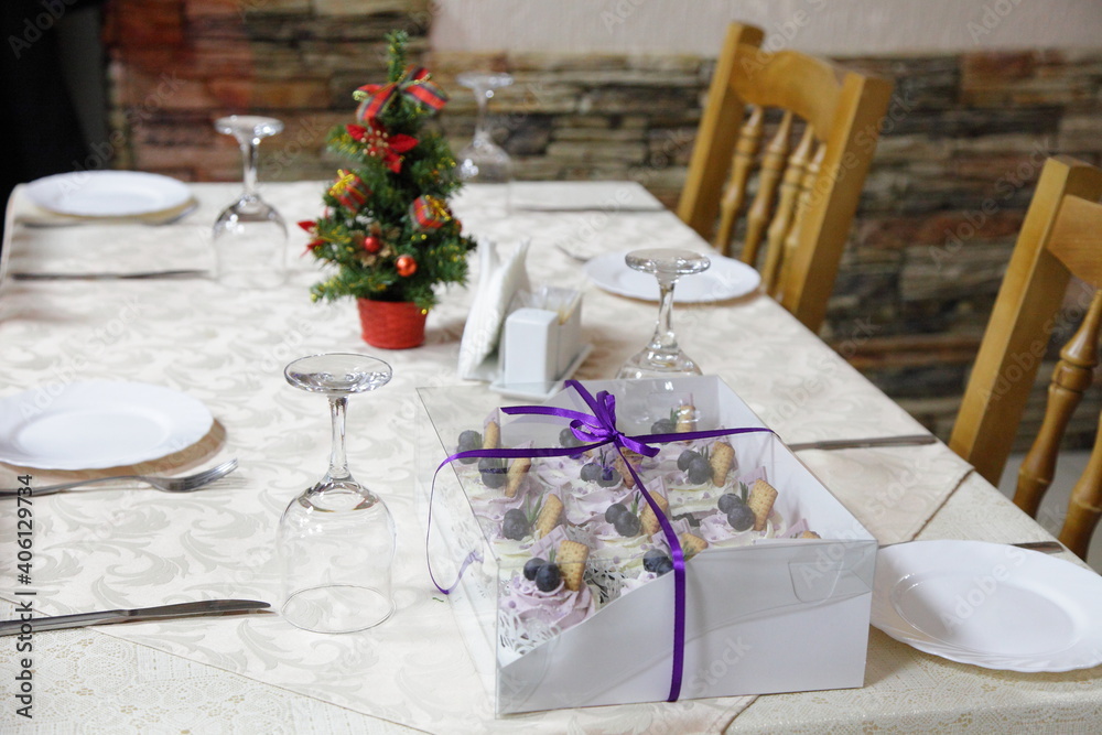 Restaurant table with cake gift, pine tree on white tablecloth and wooden chairs in empty hall, holiday in European winter cafe interior Restaurant table with cake gift, pine tree on white tablecloth and wooden chairs in empty hall, holiday in European winter cafe interior