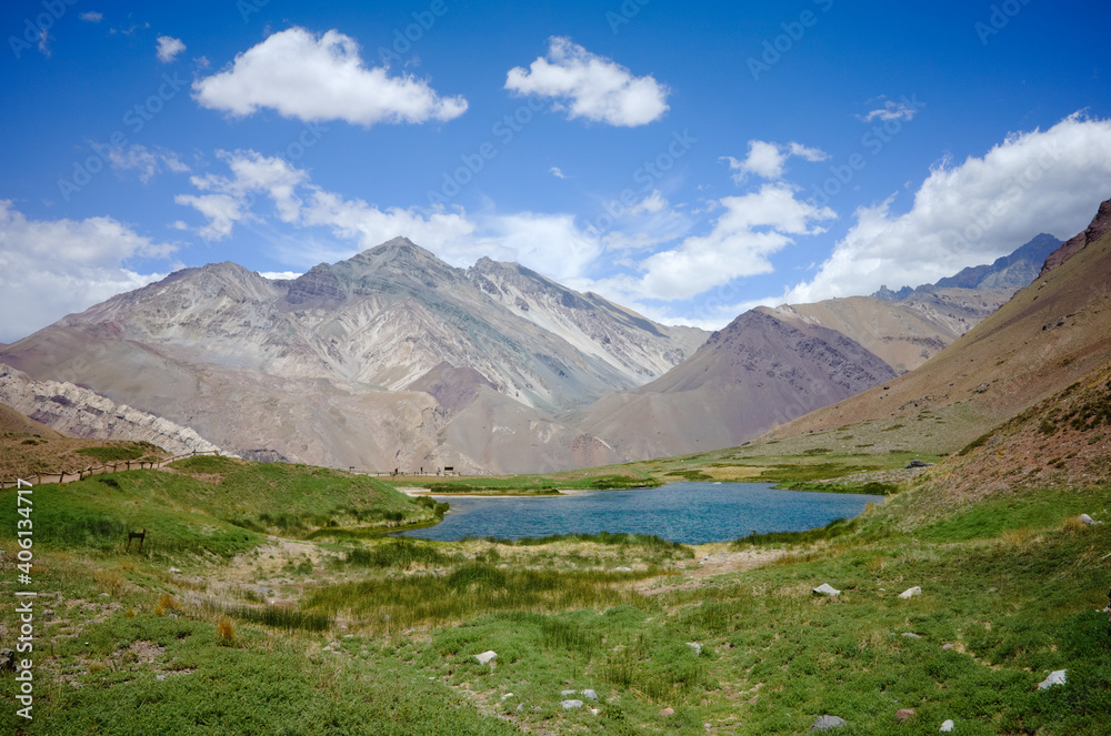 Laguna de Horcones sunny day on a hiking trail. Lake in Andes mountains with green grass around. Blue sky with clouds over hills. Aconcagua Provincial Park, Mendoza province, Argentina