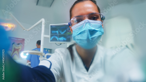 Dentist leaning over patient putting oxigen mask before surgery in stomatological office. Doctor working in modern orthodontic clinic wearing protection mask and gloves during heatlhcare checking