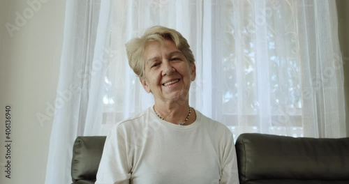 A nice elderly woman after retirement cut short hair with light brown hair smile and greet by waving her hand in a cheerful mood at her home alone.