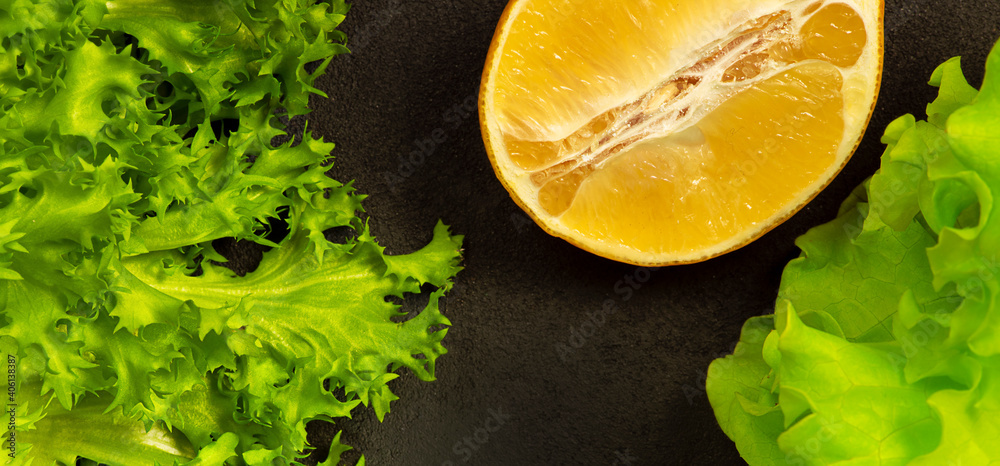 Green lettuce leaves and lemon on a dark background. Green lettuce leaves and lemon on a dark background.
