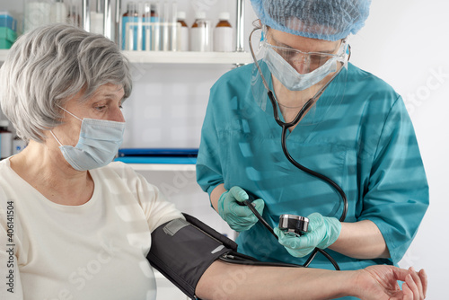 Female nurse measuring blood pressure to adult lady senior woman in the hospital