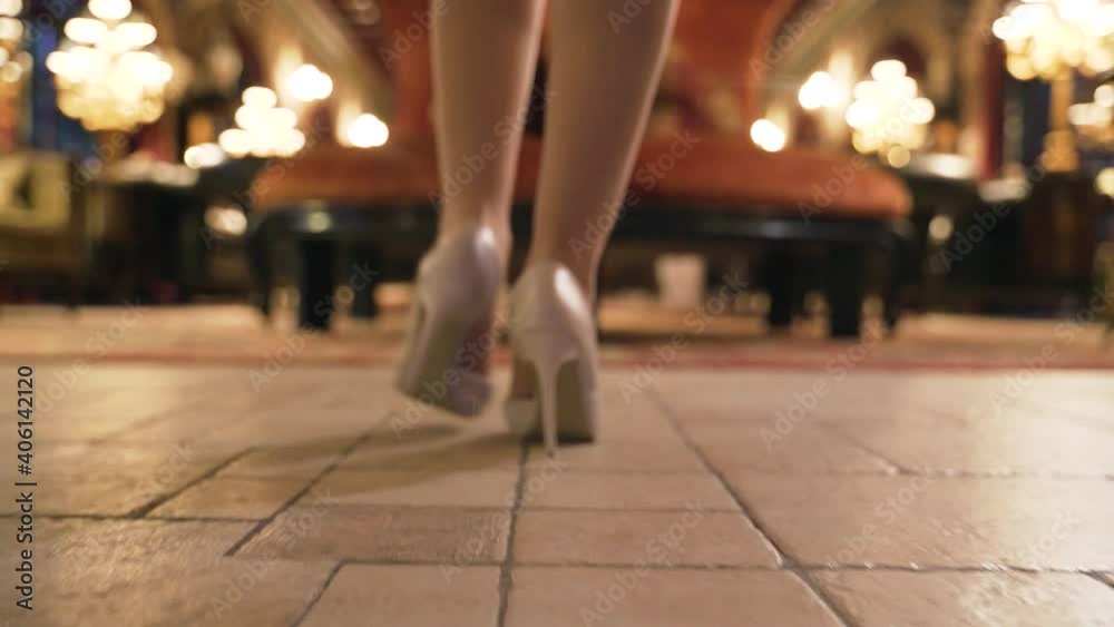 Woman with slender legs in white high heels walks on tile in restaurant Woman with slender legs in white high heels walks on tile in restaurant