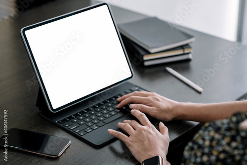 Close up. Woman hand typing on digital tablet keyboard with blank screen on desk at office.