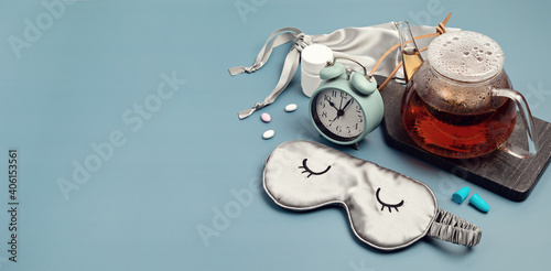Classic alarm clock, sleeping mask, tea pot on blue pastel background.  Minimal concept of rest, quality of sleep, good night, insomnia, relaxation.